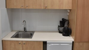 A compact kitchen with wooden cabinets, a stainless steel sink, a coffee maker, and a white dishwasher. - Athens Ianos B by Super Host Hub (Athens)