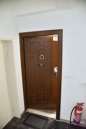 Uma porta marrom com uma placa, um extintor de incêndio e um pequeno degrau que leva à porta.
