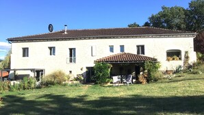 Una casa de piedra con techo de tejas, un porche cubierto y un pequeño jardín.