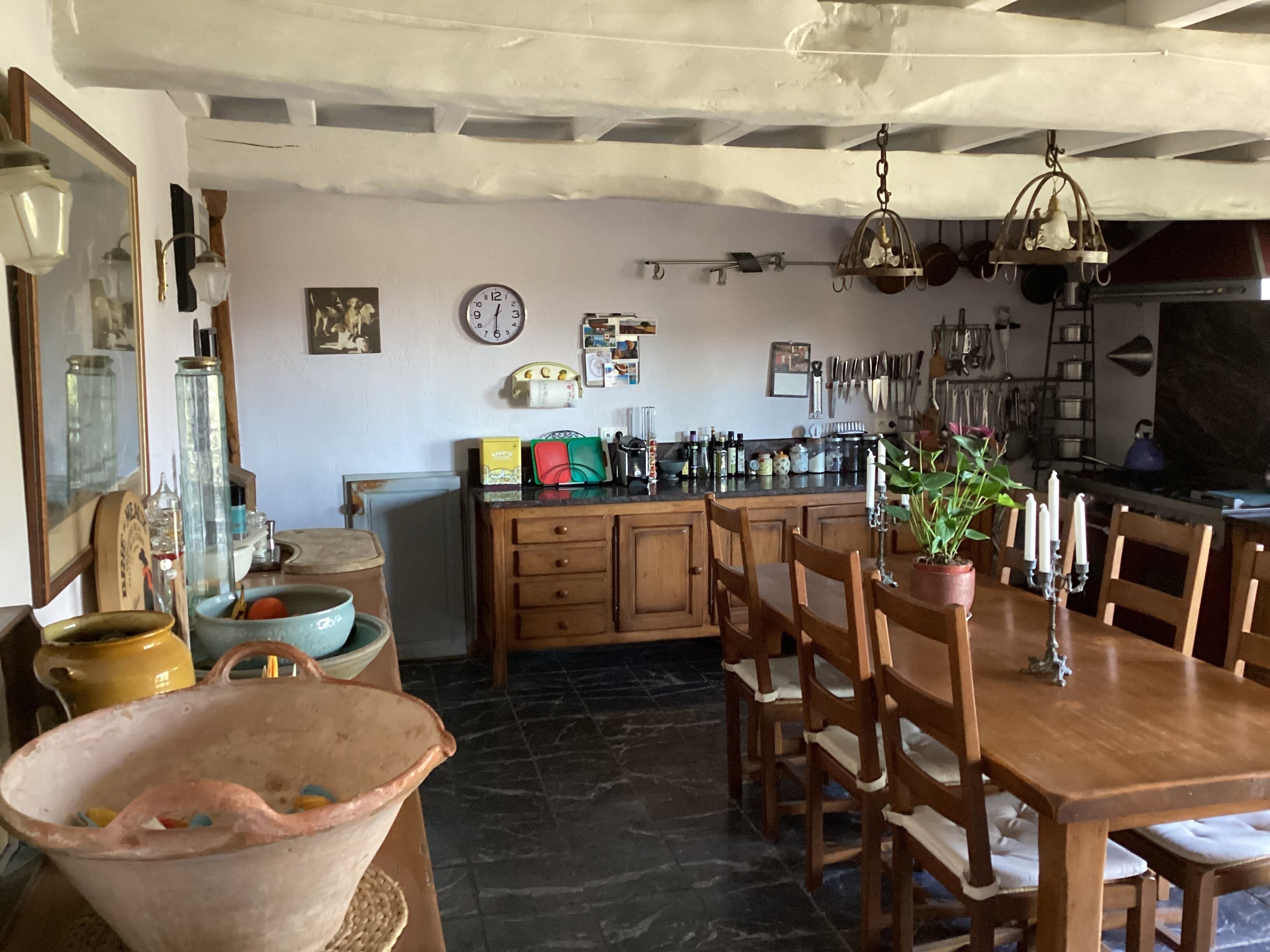 A kitchen with wooden cabinets, a dining table with chairs, a hanging light fixture, and various kitchen utensils.