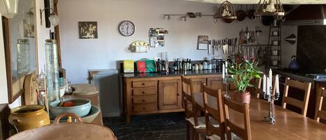 A kitchen with wooden cabinets, a dining table with chairs, a hanging light fixture, and various kitchen utensils.