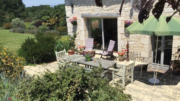 Una casa de piedra con un patio, mobiliario exterior y vistas a la vegetación circundante.