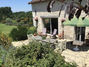 Una casa de piedra con un patio, mobiliario exterior y vistas a la vegetación circundante.
