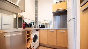 A compact kitchen with a built-in washing machine, stainless steel appliances, and wooden cabinets. - TheBlueStay 317 - Superb Apt near the Eiffel Tower (Paris)