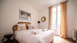 A neatly made bed with white linens, a round mirror, and a framed picture on the wall. - TheBlueStay 317 - Superb Apt near the Eiffel Tower (Paris)