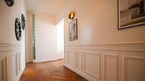 A hallway with wooden herringbone flooring, white wainscoting, and decorative wall art. - TheBlueStay 317 - Superb Apt near the Eiffel Tower (Paris)