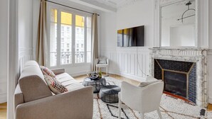 Ein geräumiges Wohnzimmer mit Kamin, einer Couch, einem Sessel, einem Couchtisch und einem an der Wand befestigten Fernseher.