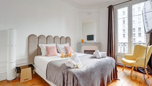 Une chambre d’hôtel moderne dotée d’un grand lit, d’une cheminée, d’une télévision et offrant une vue sur la ville grâce à de grandes fenêtres.