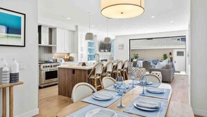 Cocina moderna con armarios blancos, una isla central y una zona de comedor con mesa de madera dispuesta para seis.