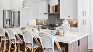 Una cocina moderna con armarios blancos, un refrigerador de acero inoxidable, una estufa a gas y una isla grande con taburetes de bar.