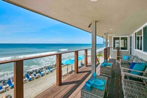 A balcony with a view of the ocean, wooden deck, and outdoor seating area with blue cushions.