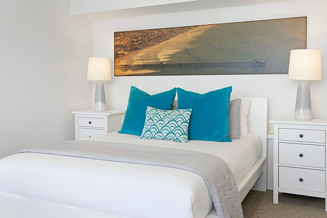 A neatly arranged bedroom with a large bed, two bedside tables, and a painting above the bed.