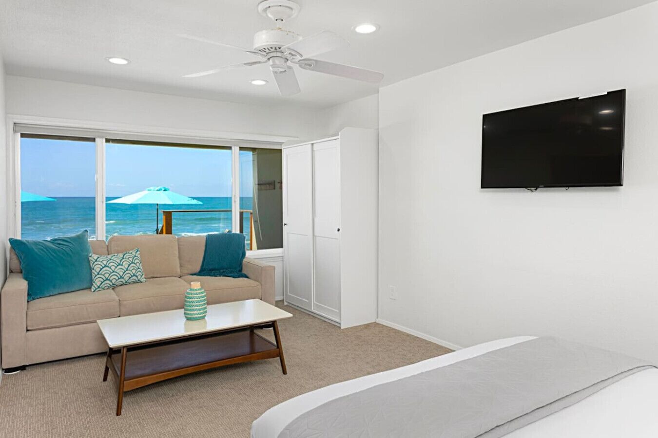 A room with a sofa, a coffee table, a TV, and a view of the ocean.