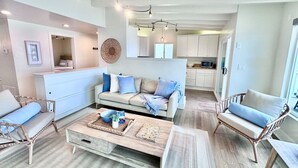 A spacious living area with a sofa, two armchairs, a coffee table, and a kitchen in the background.