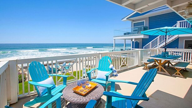 A balcony with blue chairs, a table with a tray, and a view of the ocean.