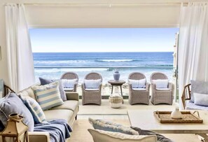 A room with a view of the ocean, featuring a sofa, two wicker chairs, a small table, and a lamp.