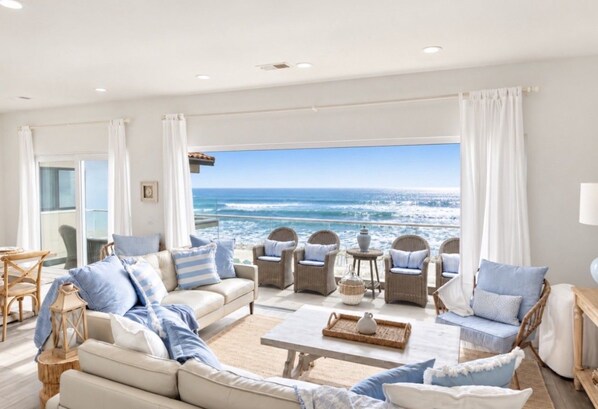 A spacious living room with a large window overlooking the ocean, furnished with sofas, chairs, and a coffee table.