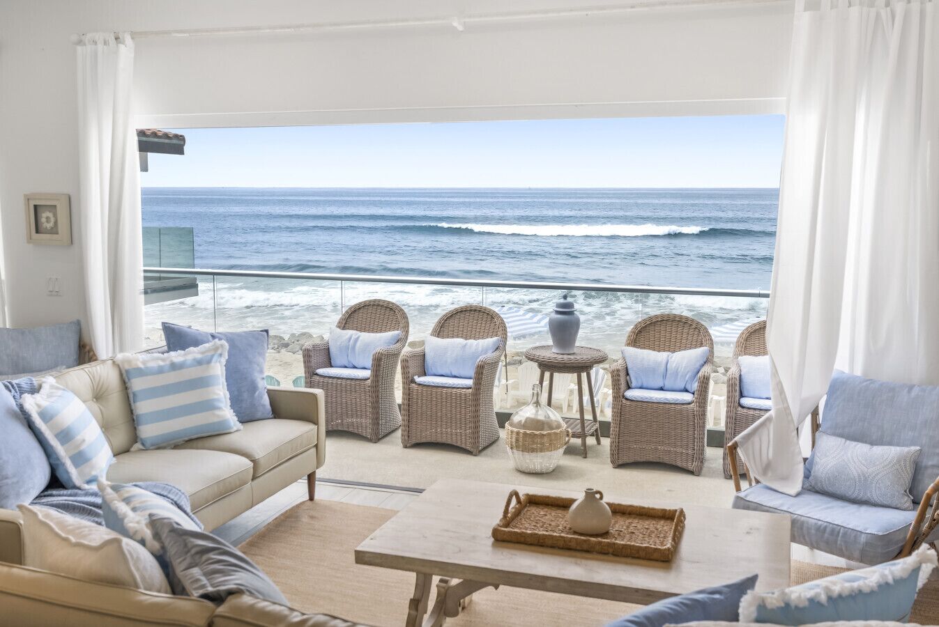 Un balcon donnant sur la plage, agrémenté de meubles en osier, d’un canapé et d’une table avec un plateau.