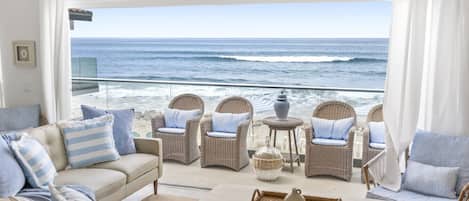 Un balcón frente a la playa con muebles de mimbre, un sofá y una mesa con una bandeja.