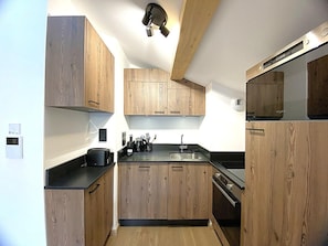 A compact kitchen with wooden cabinets, a black countertop, and a built-in microwave.