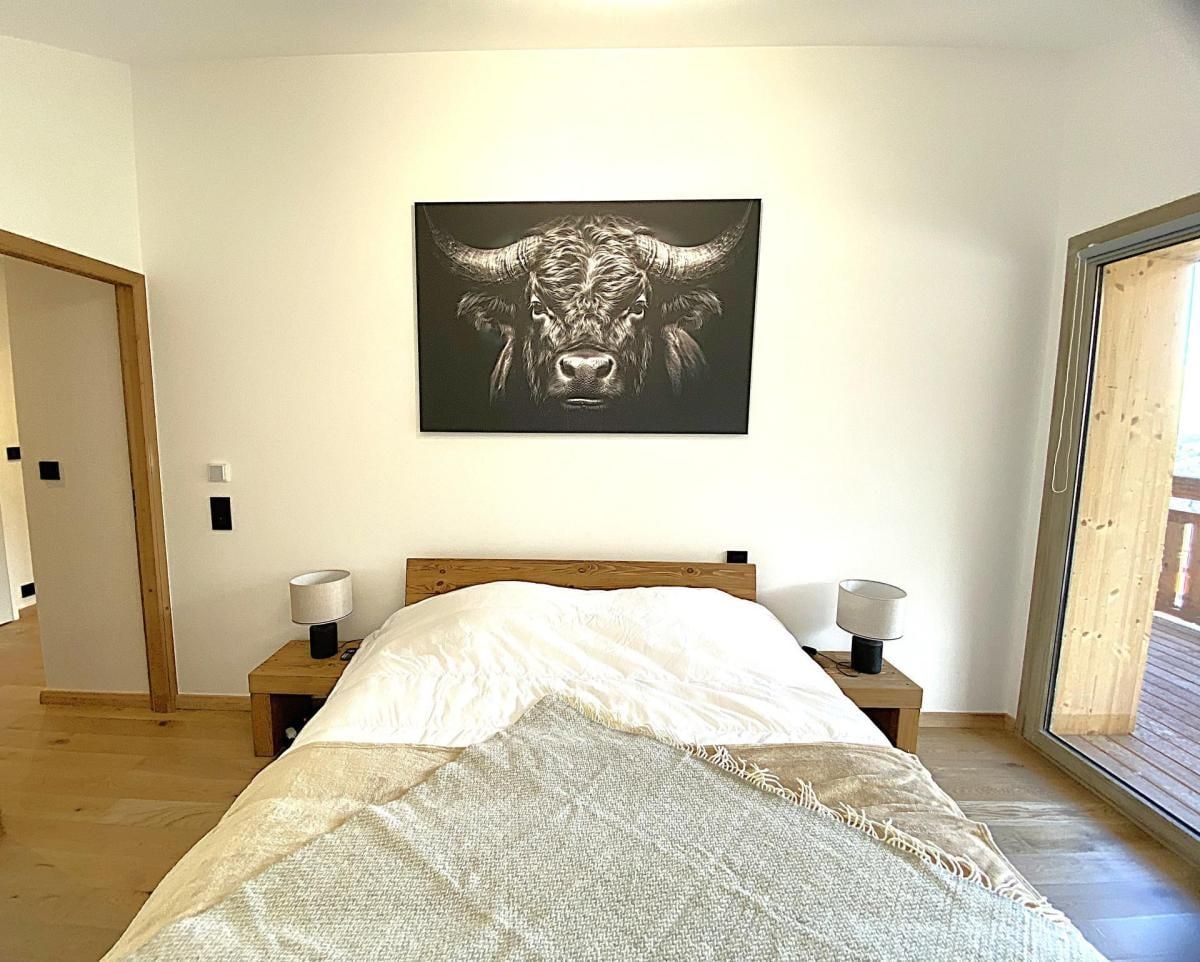A bedroom with a bed, two bedside tables with lamps, a large window, and a bull-themed artwork on the wall.