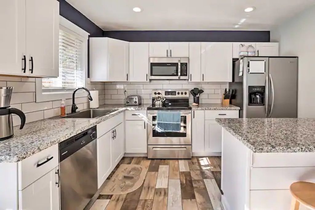 A modern kitchen with white cabinets, a stainless steel dishwasher, a built-in oven, a microwave, and a refrigerator.