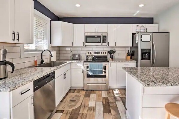 A modern kitchen with white cabinets, a stainless steel dishwasher, a built-in oven, a microwave, and a refrigerator.