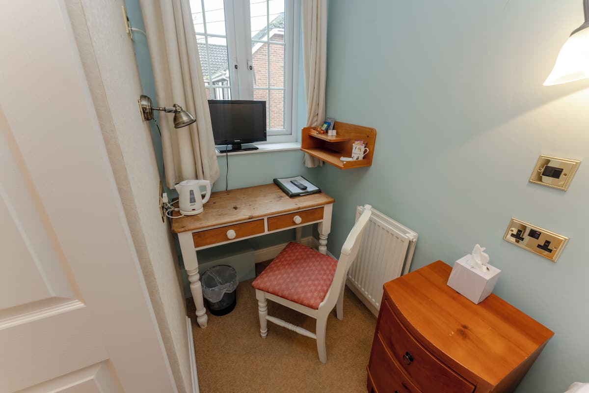 A bedroom with a wooden desk, a chair, a television, a shelf with a cup and tissues, and a radiator.