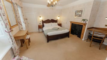 A bedroom with a wooden bed, a desk, a chair, a fireplace, and a chandelier.