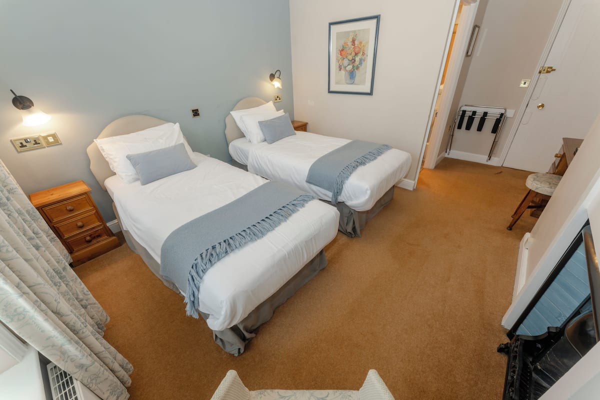 A room with two beds, a nightstand, a wall-mounted light, and a door with a towel rack.