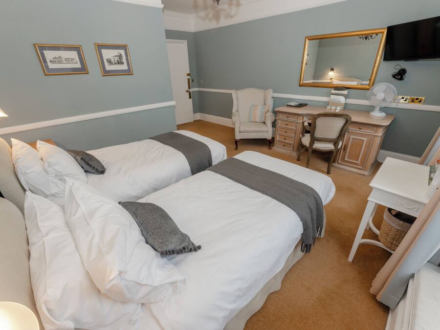 A hotel room with two beds, a desk with a chair, a dresser, a mirror, and a television.