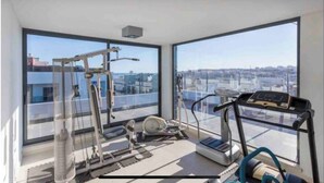 A modern gym with exercise equipment and large windows offering city views. - Modern 2Bed Rooftop Pool & Gym, Marina & Half Beach (Lagos)