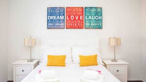 A neatly made bed with two pillows, a white nightstand with a lamp, and motivational posters on the wall. - Modern 2Bed Rooftop Pool & Gym, Marina & Half Beach (Lagos)