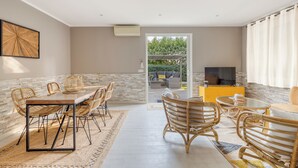 A spacious living area with a dining table, wicker chairs, and a sofa. There is a TV and a yellow cabinet in the background.