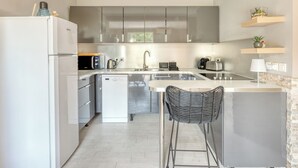 A modern kitchen with stainless steel appliances, a dishwasher, and a bar area with two stools.