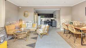 A spacious living area with a sofa, chairs, a coffee table, and a dining table. A kitchen is visible in the background.
