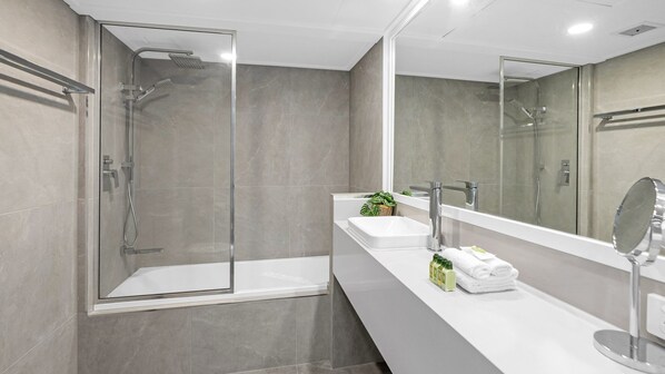 Un baño moderno con ducha envuelta en vidrio, una bañera independiente y un tocador con espejo.