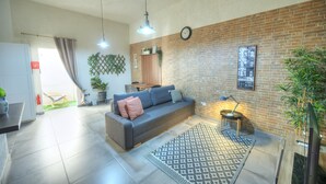 Un salon moderne avec un canapé gris, un tapis à motifs, un mur en briques et une horloge.