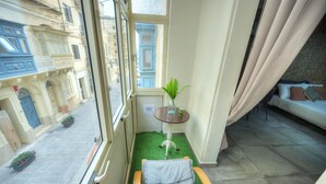 Un petit balcon avec un lit, une plante en pot et une vue sur une rue bordée d’immeubles.