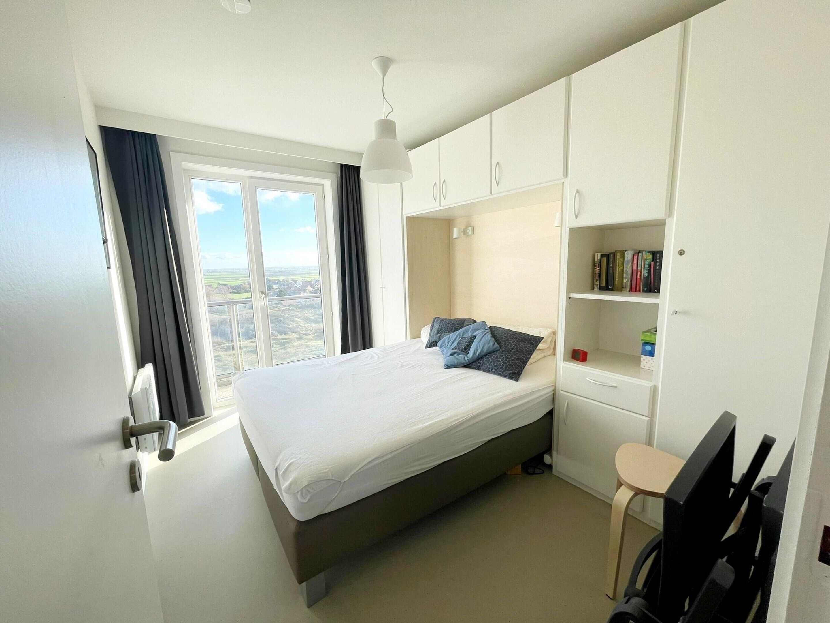 A bedroom with a bed, a desk, a chair, a bookshelf, and a window with curtains.