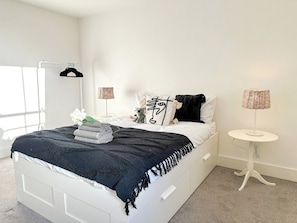 A bedroom with a bed, a bedside table, a lamp, a hanging rack, and a window. - *New* | St James - City Centre Modern Apartment (Canterbury)
