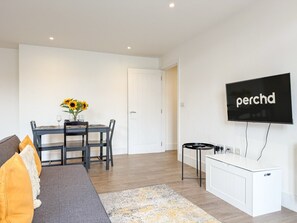 Een moderne woonkamer met een bank, eettafel en een aan de muur bevestigde flatscreen-tv.