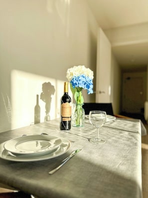 A dining table with a bottle of wine, a glass, and a vase of flowers. - *New* | St James - City Centre Modern Apartment (Canterbury)