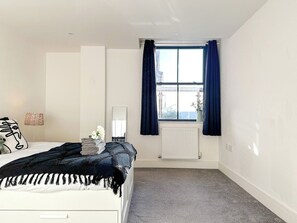 A bedroom with a bed, a window with curtains, a radiator, and a wall-mounted mirror. - *New* | St James - City Centre Modern Apartment (Canterbury)