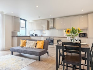 A modern kitchen with white cabinets, a grey sofa, and a dining table with chairs. - *New* | St James - City Centre Modern Apartment (Canterbury)