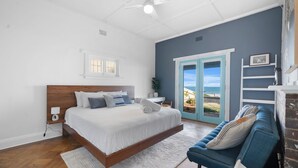 Een slaapkamer met een groot bed, uitzicht op de oceaan door een deur, een blauwe bank en een witte muur.