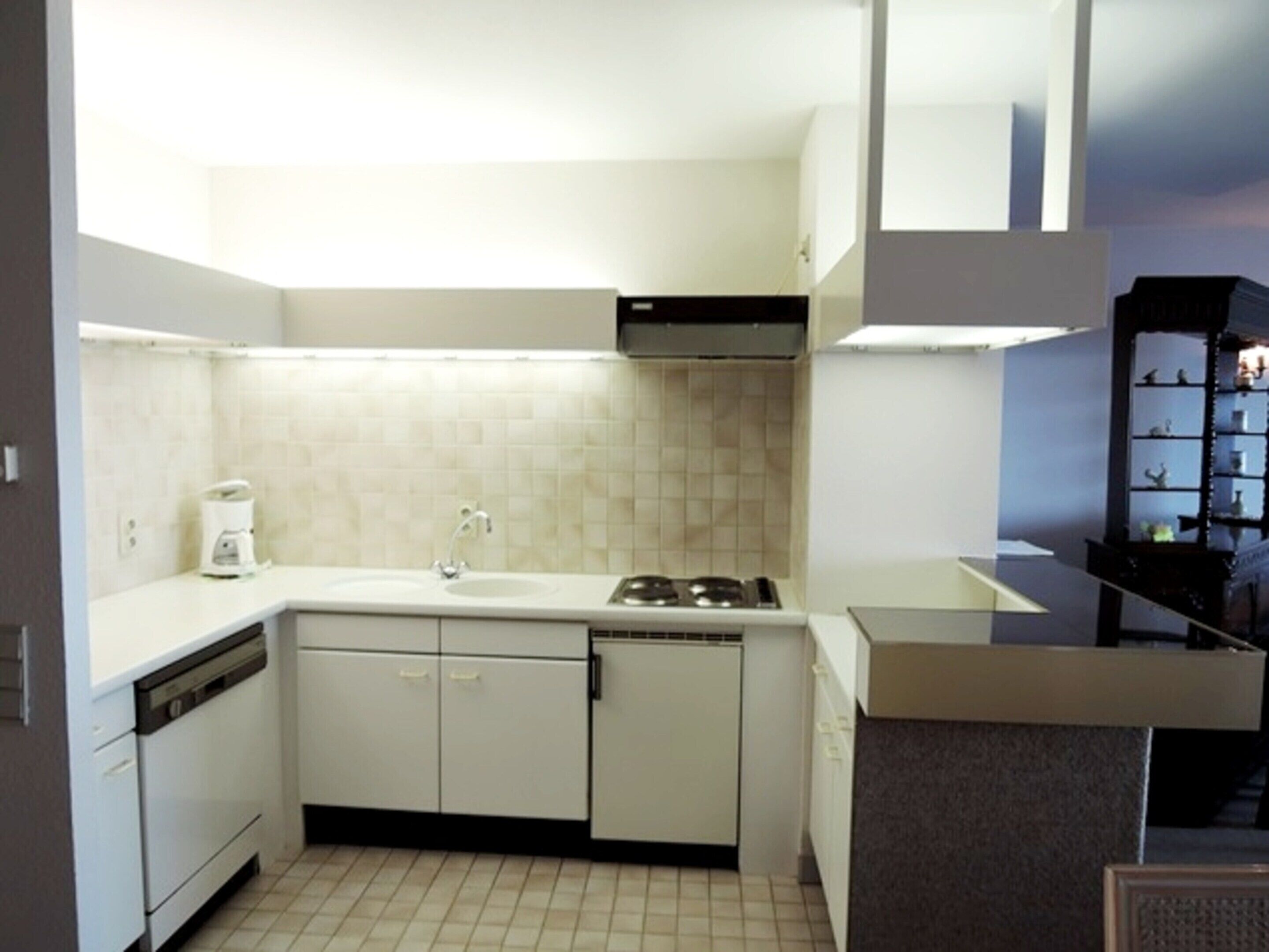 Una cocina compacta con armarios blancos, lavavajillas, estufa y cafetera.
