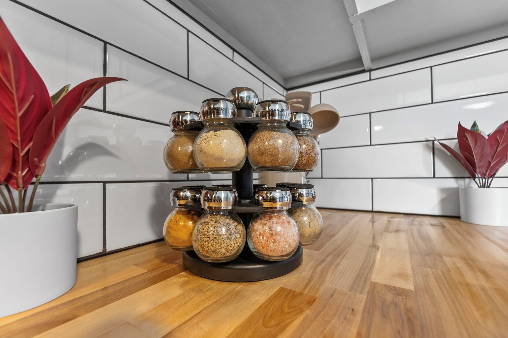A spice rack with multiple glass jars on a rotating stand in a kitchen.
