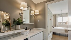 A modern bathroom with a large mirror, two wall-mounted lamps, a sink, and a potted plant. - OLA LIVING ST ANTONI 17 (Barcelona)