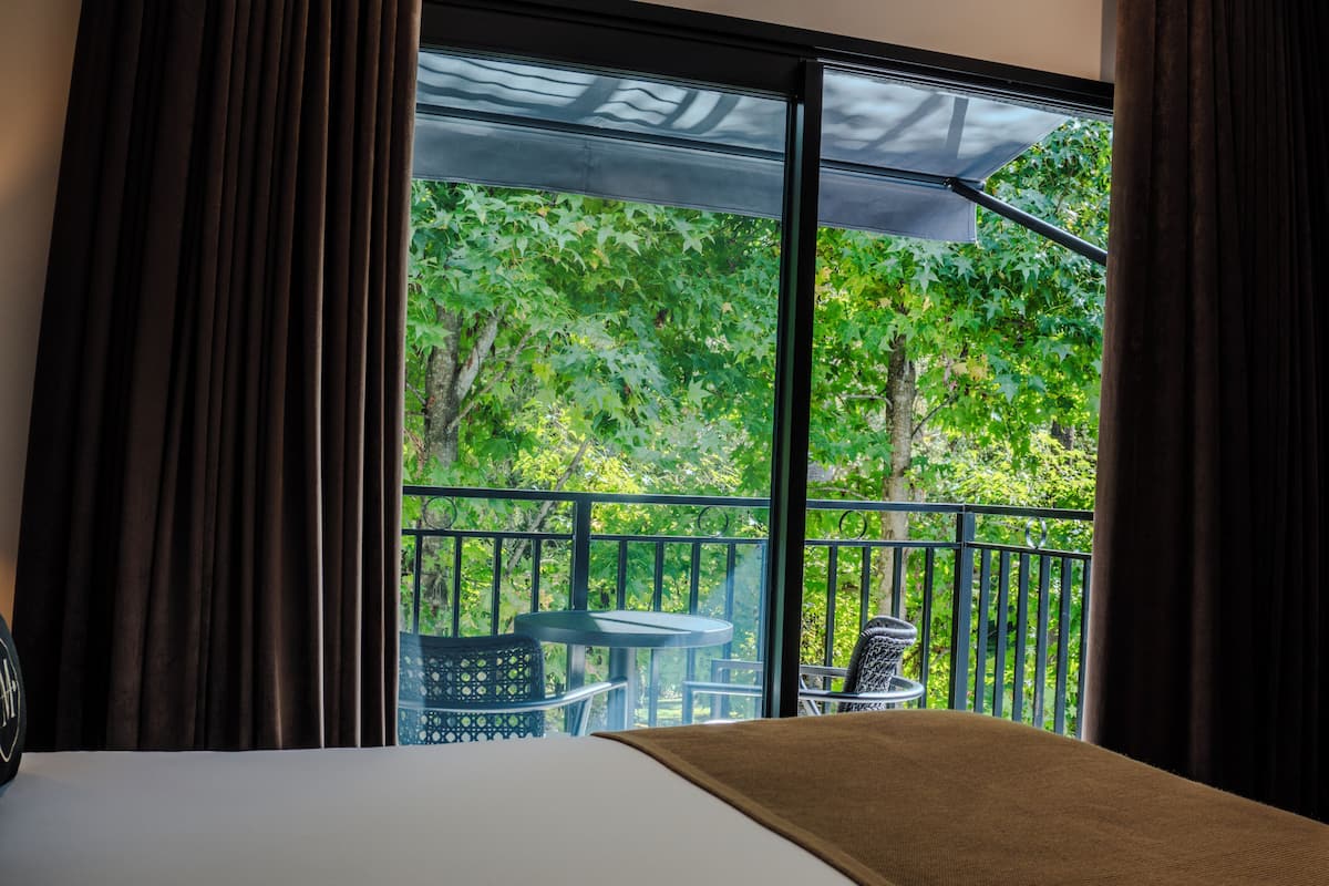 Ein Hotelzimmer mit großem Fenster, einem Bett und einem Balkon mit Tisch und Stühlen.